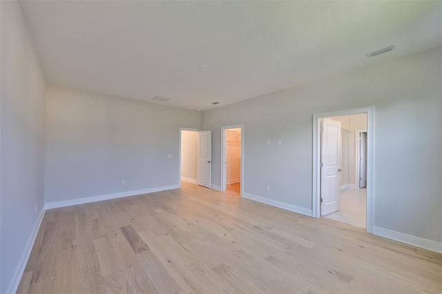 empty room with light wood-type flooring, visible vents, and baseboards