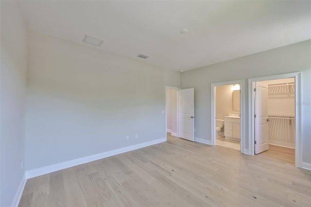 unfurnished bedroom with a walk in closet, baseboards, visible vents, and light wood-type flooring