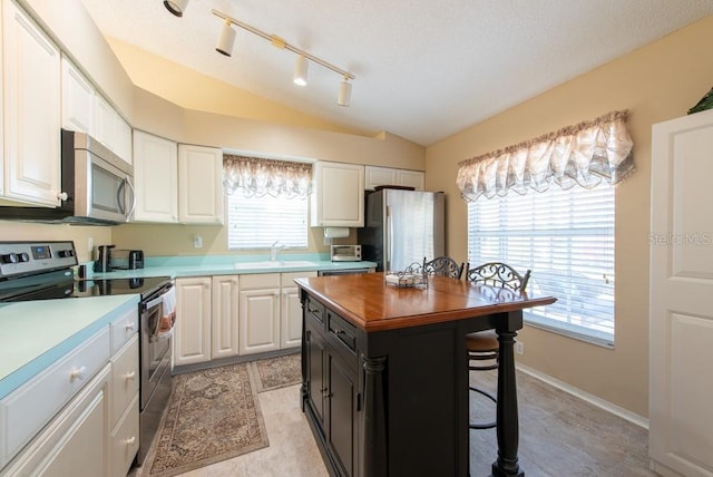 kitchen featuring a breakfast bar, a sink, white cabinetry, appliances with stainless steel finishes, and vaulted ceiling