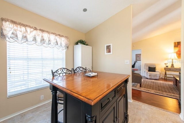 kitchen featuring baseboards, a breakfast bar, lofted ceiling, light wood-style flooring, and open floor plan