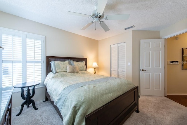 carpeted bedroom featuring visible vents, baseboards, a closet, a textured ceiling, and a ceiling fan