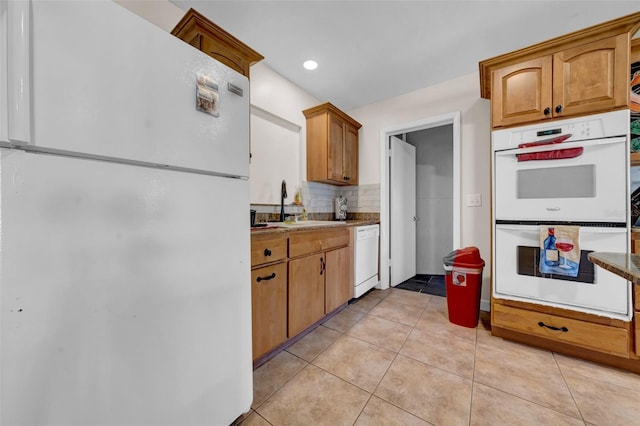 kitchen featuring white appliances, light tile patterned floors, a sink, brown cabinets, and backsplash
