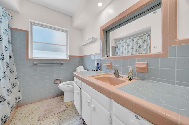 bathroom with vanity, speckled floor, wainscoting, tile walls, and toilet