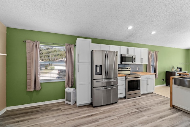 kitchen featuring white cabinetry, light wood-style flooring, tasteful backsplash, and stainless steel appliances