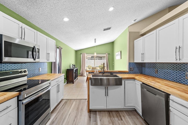 kitchen with a sink, vaulted ceiling, stainless steel appliances, and butcher block counters