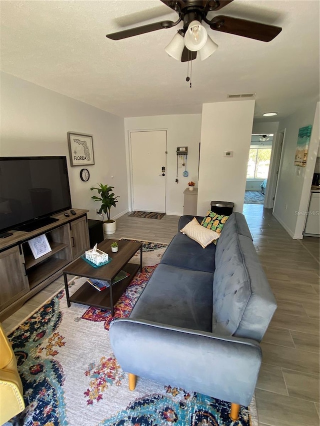 living room featuring wood finished floors, a ceiling fan, visible vents, baseboards, and a textured ceiling