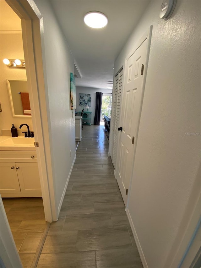 corridor with wood finish floors, baseboards, and a sink