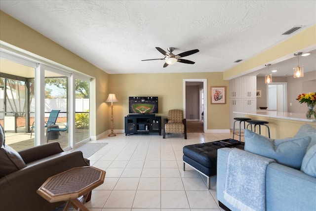 living room with light tile patterned floors, visible vents, a textured ceiling, and a ceiling fan