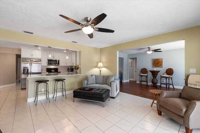 living room featuring light tile patterned flooring, visible vents, a textured ceiling, and a ceiling fan