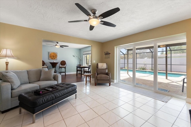 living room with light tile patterned flooring, a ceiling fan, baseboards, and a textured ceiling