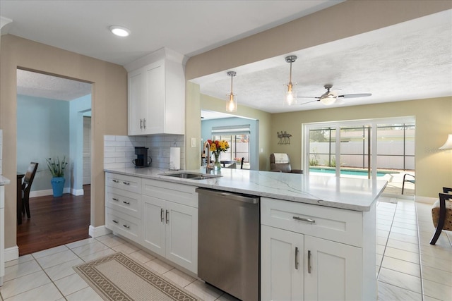 kitchen featuring dishwasher, light tile patterned floors, a peninsula, white cabinets, and a sink