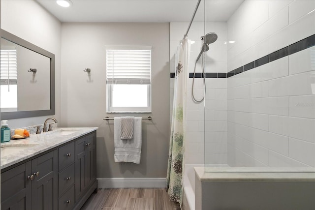 bathroom featuring wood finished floors, baseboards, double vanity, a tile shower, and a sink