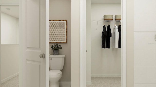 bathroom with baseboards, toilet, and a spacious closet