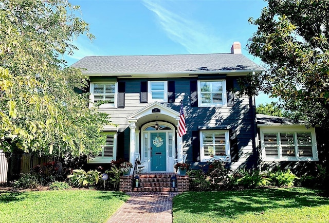 colonial-style house featuring a front lawn, fence, and a chimney