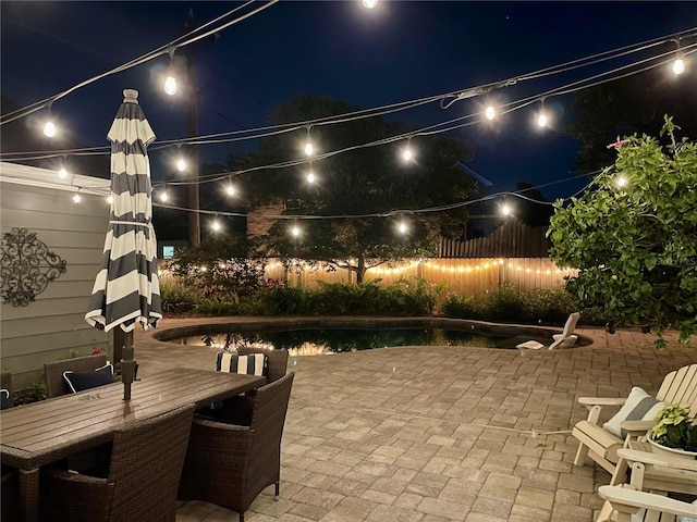 patio at night featuring outdoor dining area, a fenced in pool, and fence