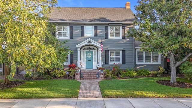 colonial-style house with a chimney, a front lawn, and roof with shingles