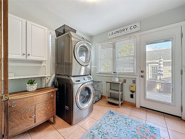 laundry area with light tile patterned flooring, cabinet space, a textured ceiling, and stacked washer and dryer