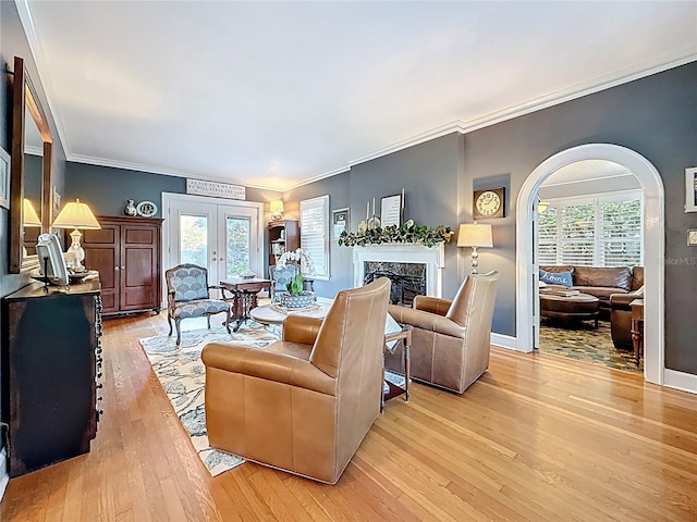 living room featuring baseboards, a premium fireplace, arched walkways, ornamental molding, and light wood-style floors