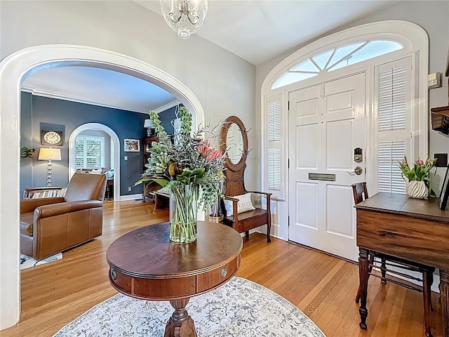 entryway with arched walkways, a notable chandelier, and light wood finished floors