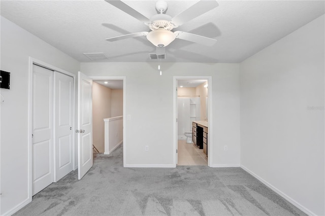 unfurnished bedroom with visible vents, baseboards, light colored carpet, a closet, and ensuite bath