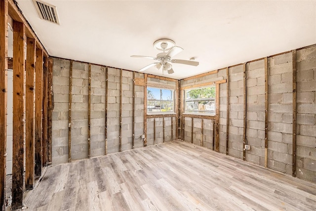 empty room featuring visible vents, concrete block wall, wood finished floors, and a ceiling fan