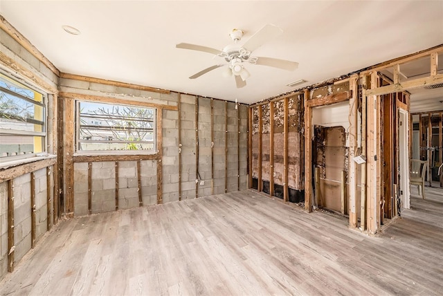 unfurnished room with visible vents, concrete block wall, wood finished floors, and a ceiling fan