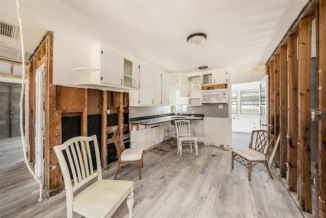 kitchen with white microwave, light wood finished floors, open shelves, white cabinets, and dark countertops