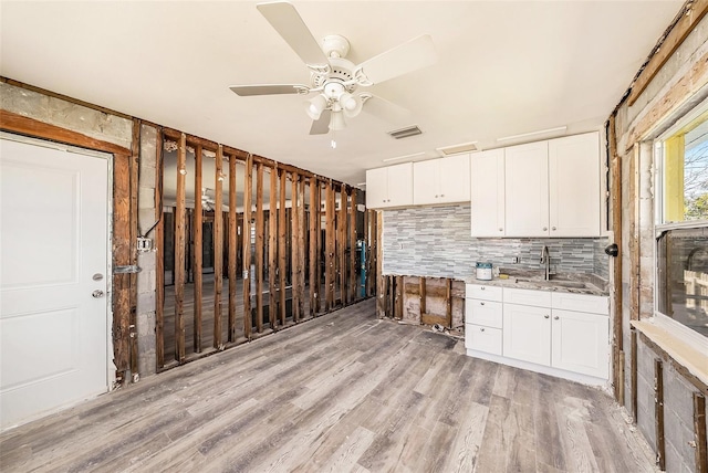 kitchen featuring visible vents, a sink, backsplash, white cabinets, and light wood finished floors