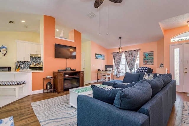 living room with a ceiling fan, vaulted ceiling, wood finished floors, and visible vents