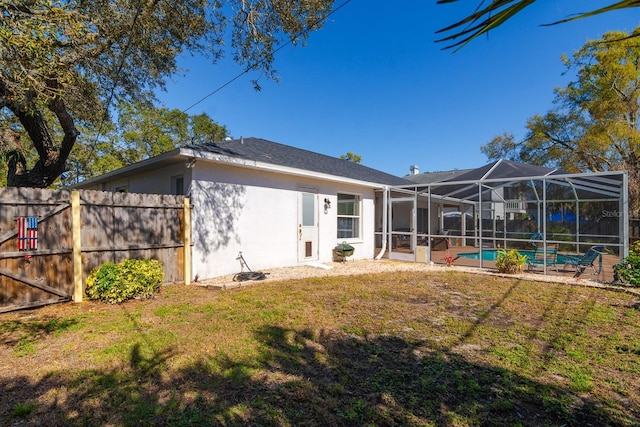 back of house with stucco siding, a lawn, fence, a fenced in pool, and a lanai