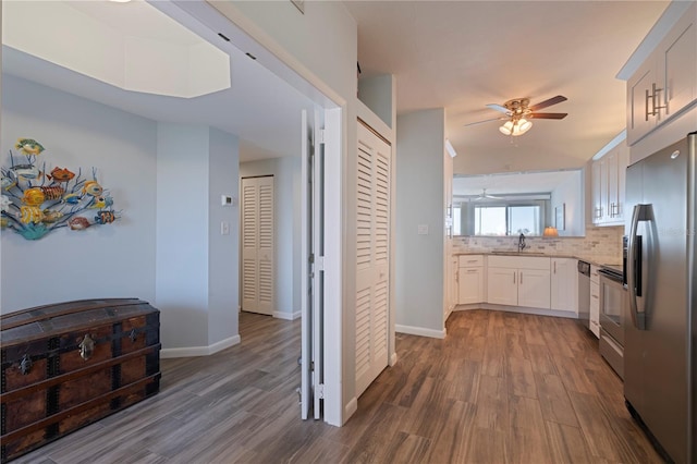 kitchen with dark wood finished floors, a sink, decorative backsplash, ceiling fan, and appliances with stainless steel finishes