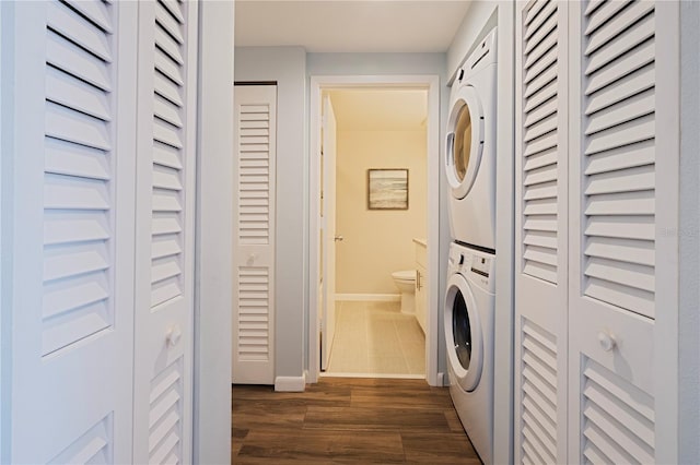 laundry room featuring estacked washer and dryer, dark wood-style flooring, and baseboards