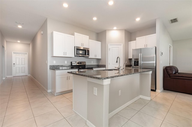 kitchen with visible vents, an island with sink, dark stone countertops, stainless steel appliances, and a sink