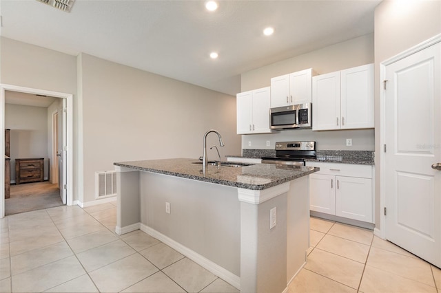 kitchen with visible vents, dark stone counters, an island with sink, a sink, and appliances with stainless steel finishes