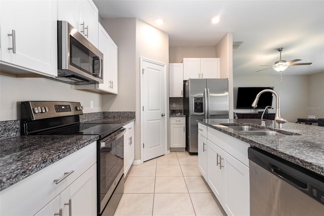 kitchen with light tile patterned floors, dark stone countertops, white cabinets, stainless steel appliances, and a sink