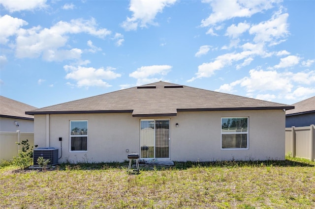 back of property with stucco siding, a lawn, central AC unit, and fence