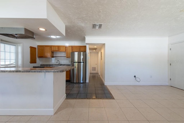 kitchen with visible vents, brown cabinets, a sink, dark countertops, and freestanding refrigerator