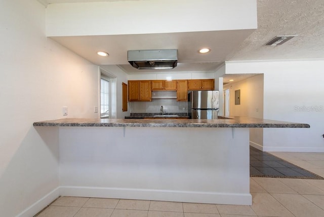 kitchen with brown cabinetry, light tile patterned flooring, freestanding refrigerator, and a sink