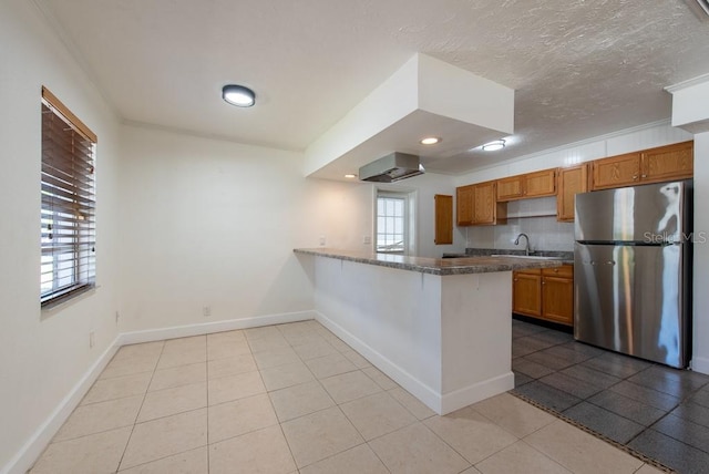 kitchen featuring baseboards, a peninsula, freestanding refrigerator, brown cabinetry, and a sink