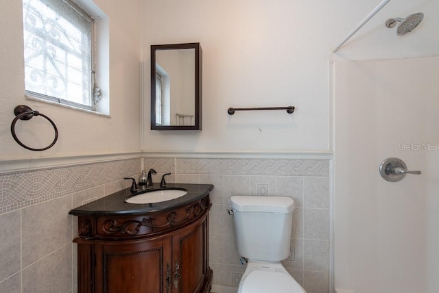 bathroom featuring vanity, wainscoting, walk in shower, tile walls, and toilet