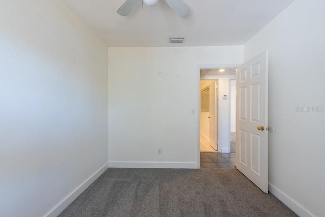 carpeted spare room with visible vents, baseboards, and ceiling fan