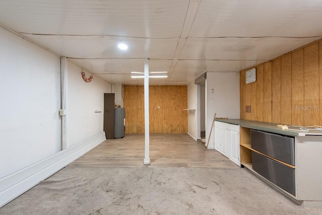 finished basement with light carpet, water heater, wood walls, and light wood-type flooring