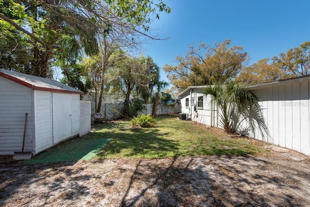 view of yard with an outdoor structure, a shed, fence, and central AC