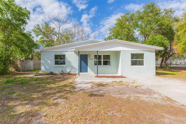 view of front of property featuring stucco siding, covered porch, driveway, and fence