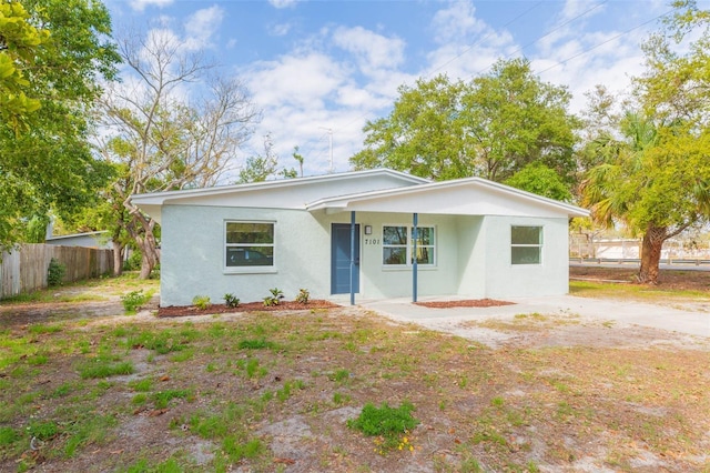 view of front facade with dirt driveway, stucco siding, and fence