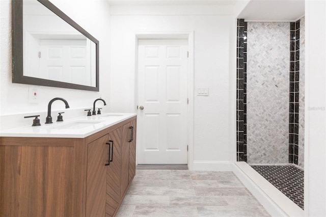 full bathroom featuring double vanity, tiled shower, and a sink