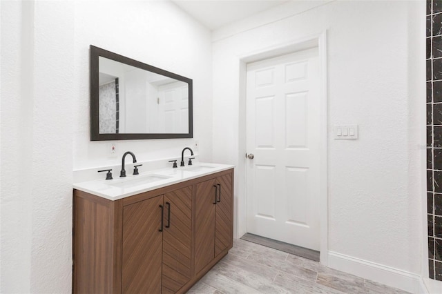 bathroom with double vanity, baseboards, wood finish floors, and a sink