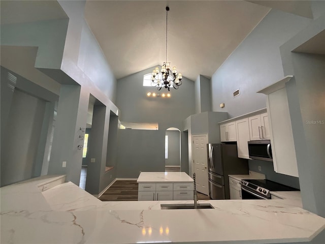 kitchen with light stone counters, a kitchen island, arched walkways, appliances with stainless steel finishes, and a notable chandelier