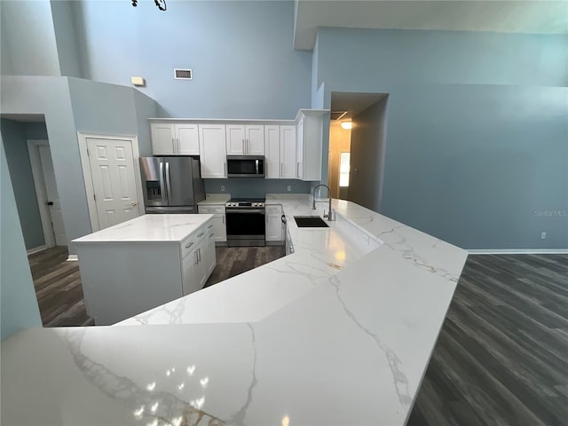 kitchen with visible vents, a center island, light stone countertops, stainless steel appliances, and a sink