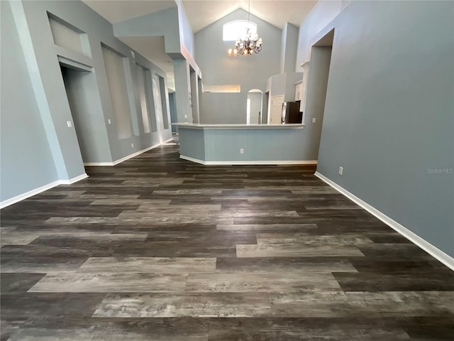 empty room featuring dark wood finished floors, a notable chandelier, high vaulted ceiling, and baseboards